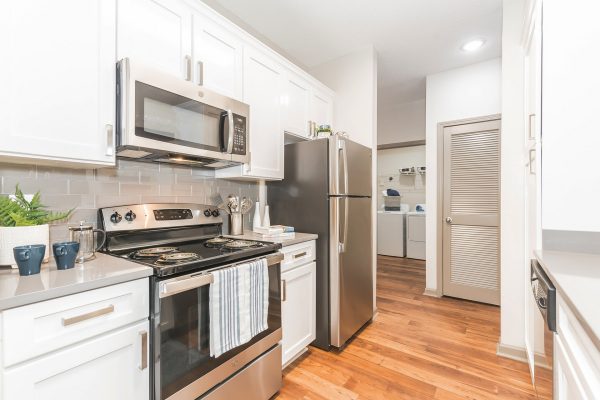 Gourmet kitchen with hardwood-style flooring, quartz countertops, white cabinetry, subway tile backsplash, and stainless steel appliances, including a microwave, stove, oven, refrigerator, and dishwasher. The laundry closet with a full-size washer and dryer can also be seen.