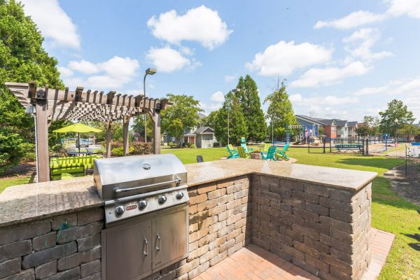 Outdoor grilling station with lots out counter space and a lounge, fire pit, playground, and fenced-in bark park in the background