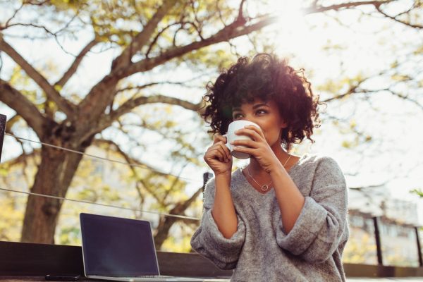 Woman sipping coffee outside while working on her laptop