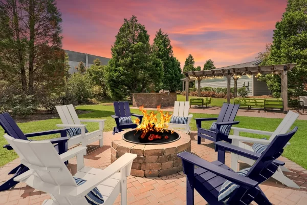Eight Adirondack chairs around a blazing fire pit with an outdoor lounge, grilling station, and a beautiful pink and orange sunset in the background